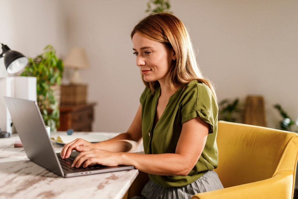 Portrait of diligent mid adult woman using laptop when working on a project, at home office.